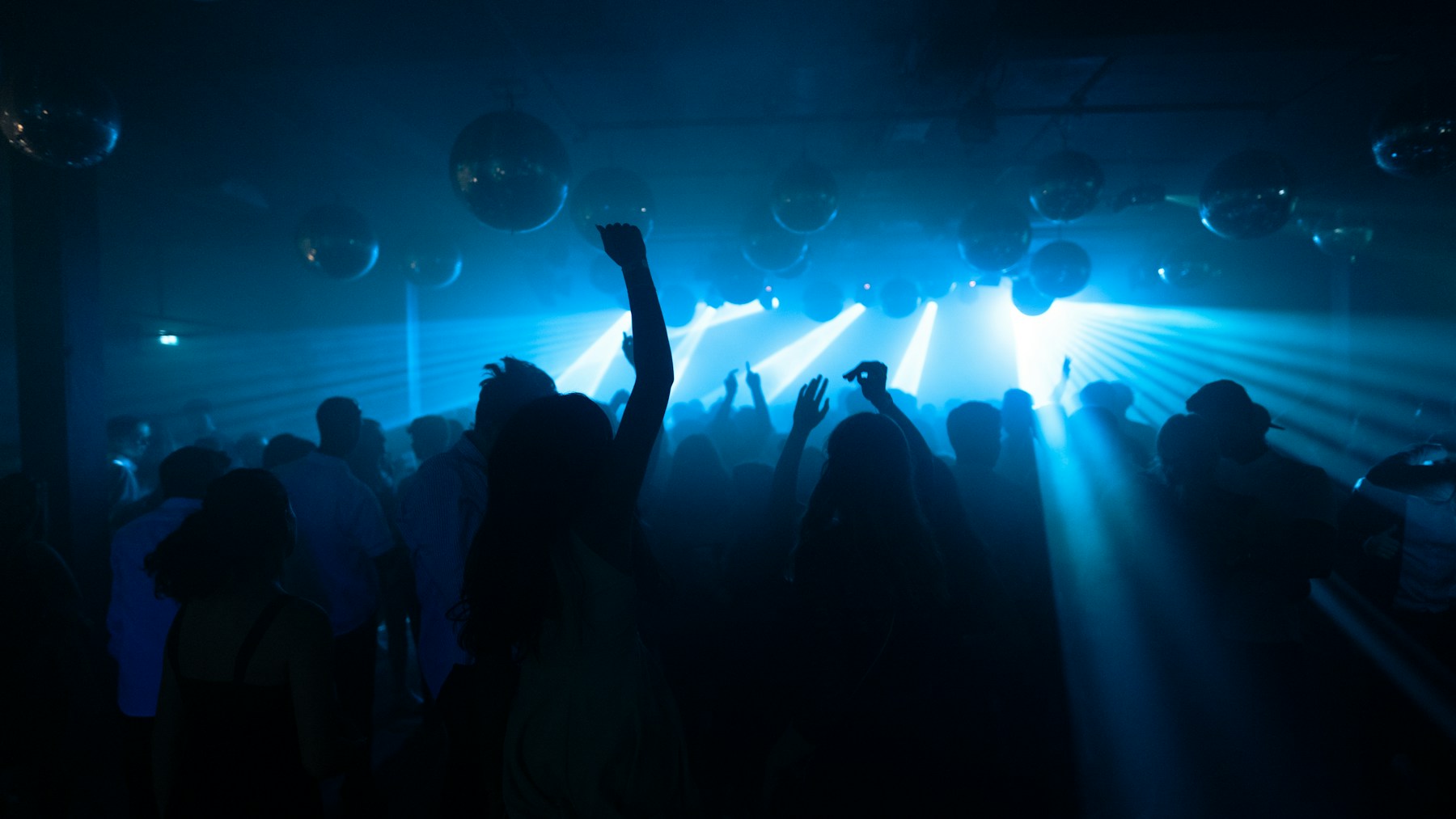 Silhouettes on a dance floor beneath mirror balls and blue light